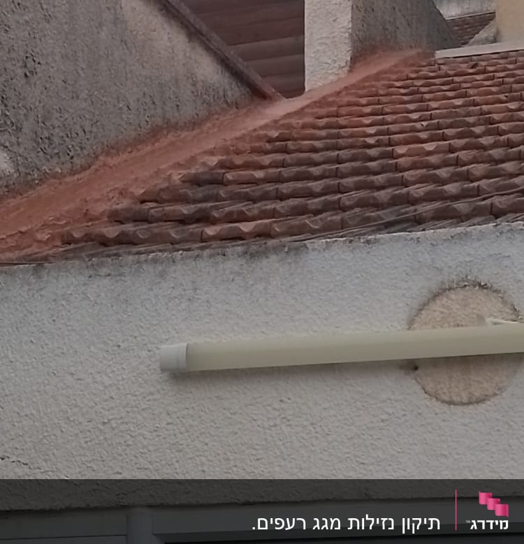 רעפים חומים על גג עם קיר בטון